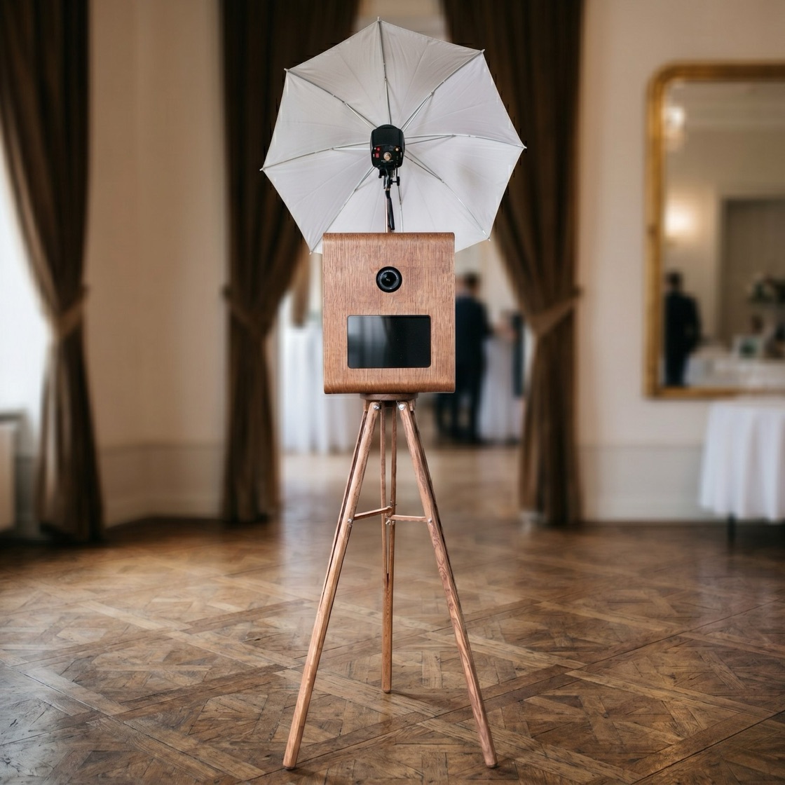 TBD's hand-built walnut photo booth on its wooden tripod, with studio flash umbrella, set up in a venue